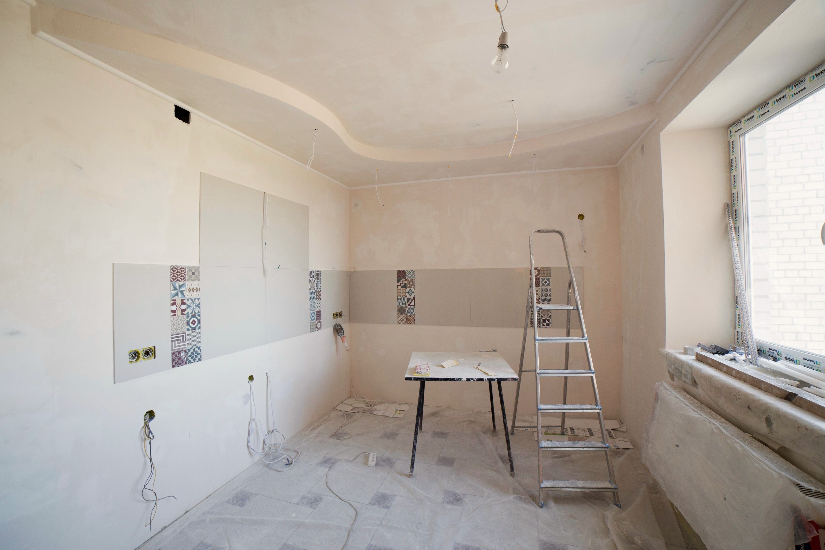Kök under renovering med spacklade väggar, stege och arbetsbord