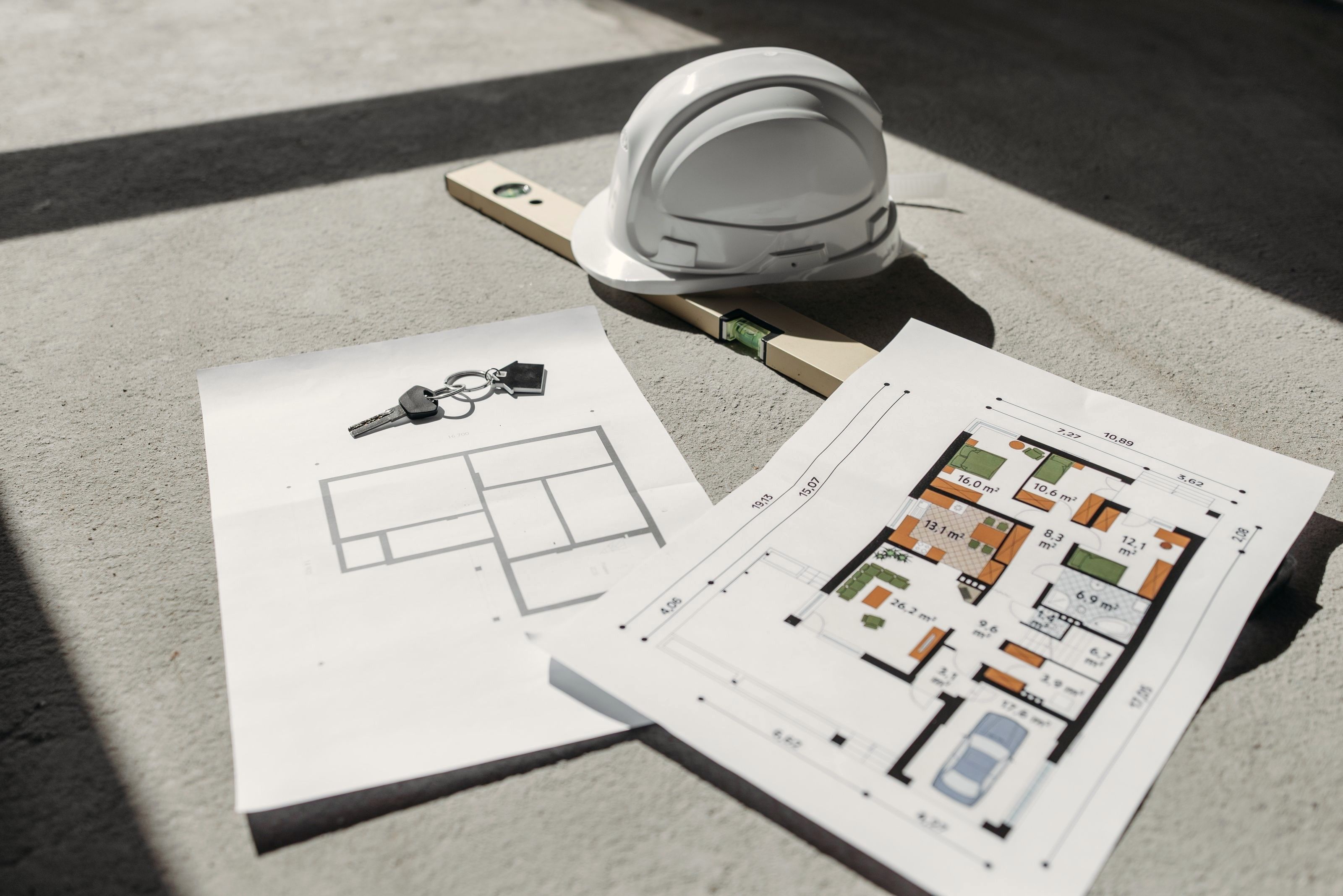 Planritningar, nycklar och en skyddshjälm på ett betonggolv